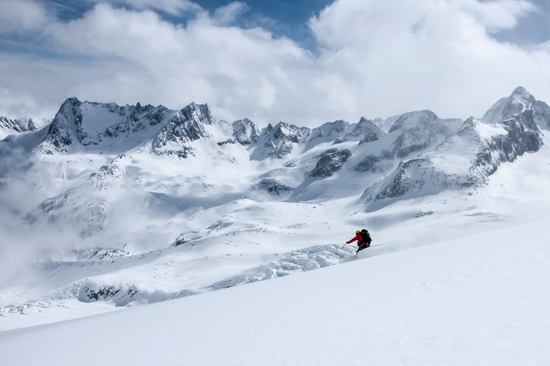 A skier in a red jacket carving down a bright slope below an icefall
